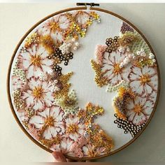 a person is holding up a cross stitch pattern on a wooden hoop with beads and sequins