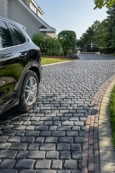 a black car parked on the side of a brick road in front of a house