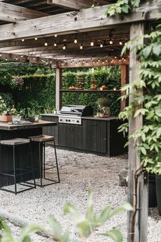 an outdoor kitchen and dining area with lights strung over the grilling area, surrounded by greenery