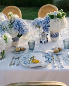 a table set with blue and white flowers in vases, plates and silverware