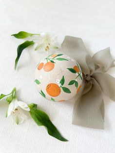 an ornament decorated with oranges and leaves on a white surface next to flowers