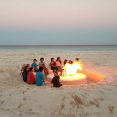 a group of people sitting around a fire pit on the beach