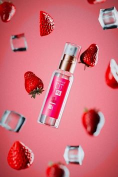 a bottle of pink liquid surrounded by strawberries and ice cubes on a pink background