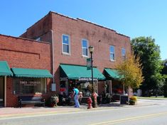 people are walking down the sidewalk in front of shops on a street corner with green awnings