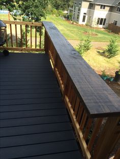 a wooden deck with black plastic flooring next to a yard and houses in the background