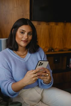 a woman sitting on a couch holding a cell phone in her hands and looking at the screen