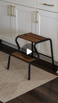 a small wooden step stool sitting on top of a rug in front of white cabinets