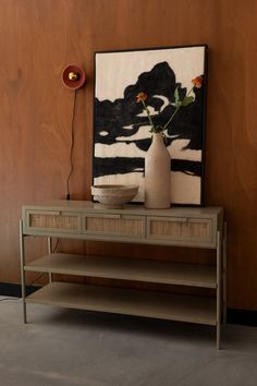 a vase with flowers sitting on top of a table next to a painting and lamp