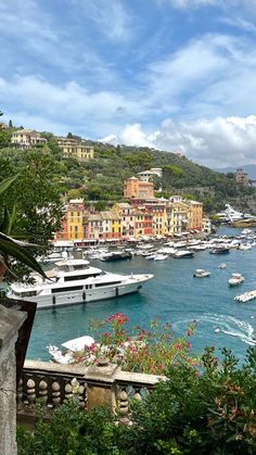 many boats are docked in the water next to some hills and buildings with trees on them