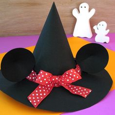 a mickey mouse hat with a red bow on it and two ghost figurines in the background