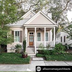 a white house with green shutters on the front porch and trees in front of it