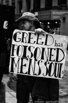 a man holding a sign that says greed has poisoned men's soul