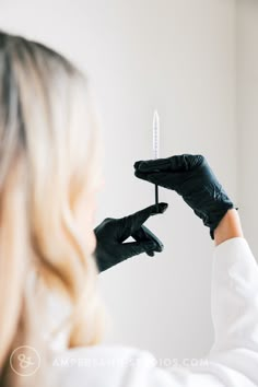 a woman in black gloves is holding a small syringe up to her face