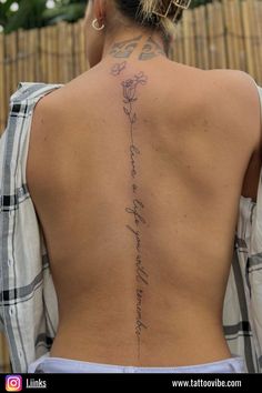 the back of a woman's body with writing on it and flowers behind her