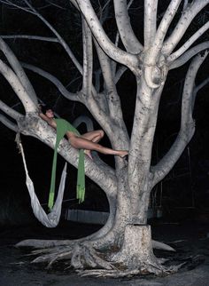 a woman sitting in a hammock hanging from a tree at night with no one around