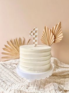 a white cake sitting on top of a table next to two gold fan shaped decorations