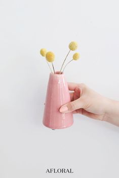 a hand holding a pink vase with yellow flowers in it and the words floral written below