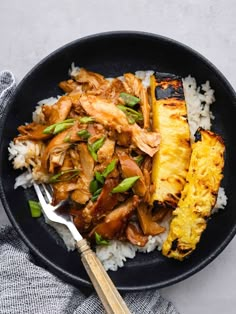 a black bowl filled with rice, meat and pineapple on top of a table