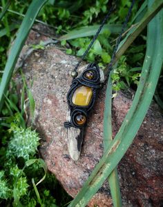 a piece of jewelry sitting on top of a rock next to some green plants and grass