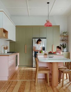 a woman and child are in the kitchen with pink cabinets, white countertops and wood floors