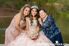 three women pose for a photo in front of a pond wearing dresses and tiaras