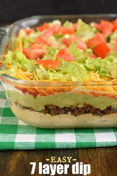 a layered salad in a glass dish on a green and white checkered tablecloth