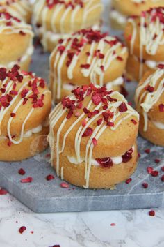 many small pastries with white icing and red sprinkles on a plate