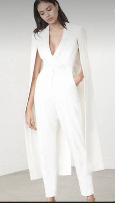 a woman is wearing a white jumpsuit with a cape over her shoulders and heels