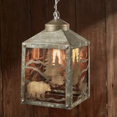 a metal lantern hanging from a chain on a wooden wall with trees in the background