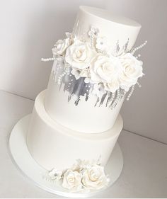 a three tiered white wedding cake with flowers on the top and side, sitting on a plate