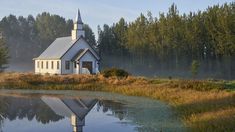 a small white church sitting on top of a lush green field next to a lake