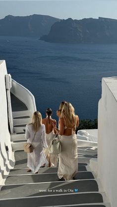 three women walking up some stairs towards the ocean