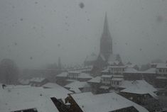 snow falling on rooftops and buildings in the distance with a church steeple in the background