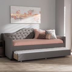 a daybed with pink and grey pillows in a living room next to a painting on the wall