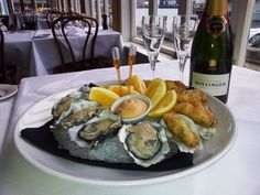 a plate with oysters, lemon wedges and some bread on it next to a bottle of wine