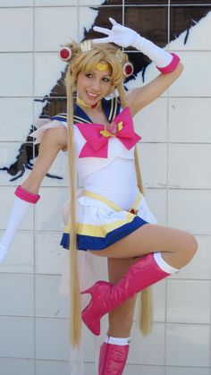 a woman with long blonde hair and pink boots posing in front of a white wall