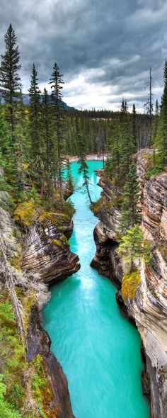 a river that is surrounded by trees and rocks in the middle of a valley with blue water