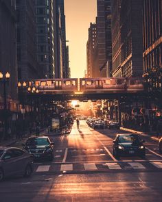 a city street with cars parked on both sides and people walking across the street at sunset