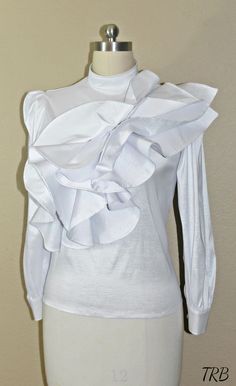 Add a high fashion statement to your wardrobe with this tiered asymmetrical ruffled Blouse. If you love being unique and the center of attention, this blouse will defiantly have all eyes on you! The low cut turtleneck neckline adds a soft, feminine touch and others will defiantly be impressed with your fashion sense. The cascade of asymmetrical ruffles across the front gives the blouse a unique wow factor. The blouse has a tailor fit and is very comfortable to wear. Made of 100% Taffeta, light w Chic Fitted Blouse With Ruffles, Chic Fitted Ruffle Blouse, Elegant Stretch Tops With Ruffles, Elegant Stretch Top With Ruffles, Elegant Ruffled Stretch Top, Elegant Evening Tops With Ruffle Hem, Elegant Evening Top With Ruffle Hem, Elegant Ruffle Hem Top For Evening, Fitted Tops With Ruffles And Ruffled Collar