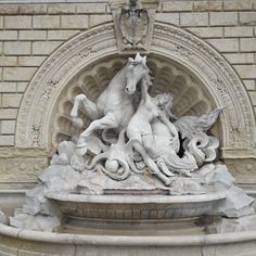 a statue of two horses on top of a fountain in front of a stone building