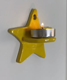 a yellow star shaped candle holder on a white wall with a silver ring around it