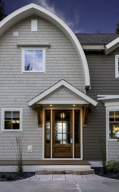 a gray house with white trim and two windows on the front door is lit up at night