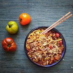 a blue bowl filled with noodles and vegetables next to tomatoes, peppers and an orange