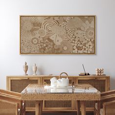 a dining room table and chairs in front of a wall with an art work on it