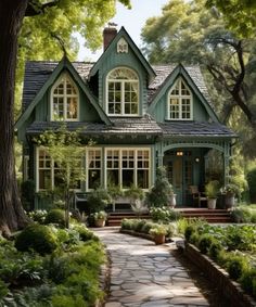 a green house with lots of windows and plants on the front lawn, surrounded by trees