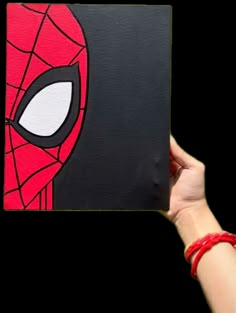 a hand holding up a black and red square with a spiderman face on it