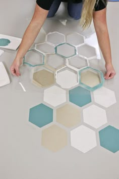 a woman kneeling down on the floor painting hexagons with blue and white paint