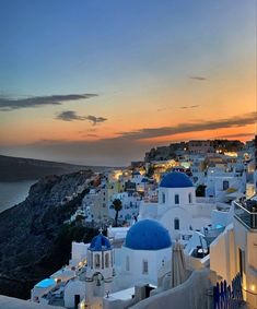 the sun is setting over some white buildings and blue domes in oia, greece