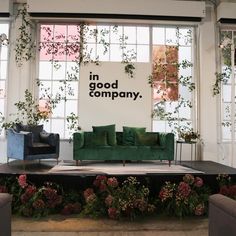 a green couch sitting on top of a stage in front of two windows with plants growing over it