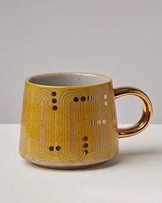 a yellow coffee cup sitting on top of a white table next to a black and gold mug